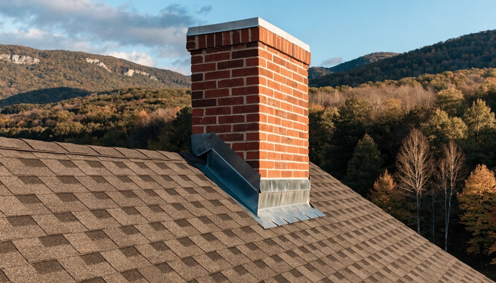 Chimney flashing repair in Stroudsburg, PA — new metal step and apron flashing sealing a brick chimney on an asphalt shingle roof in the Poconos