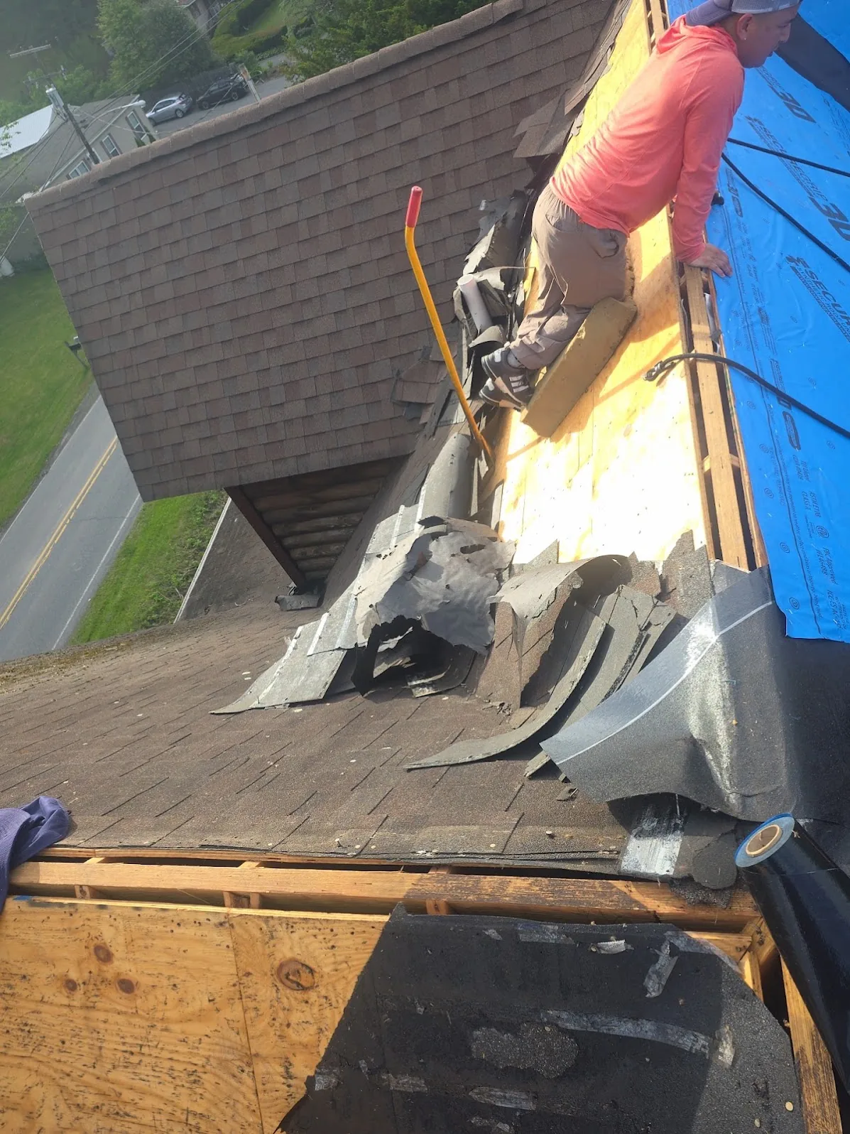 Roof tear-off in progress with the old wood decking exposed and new underlayment already down on the next section