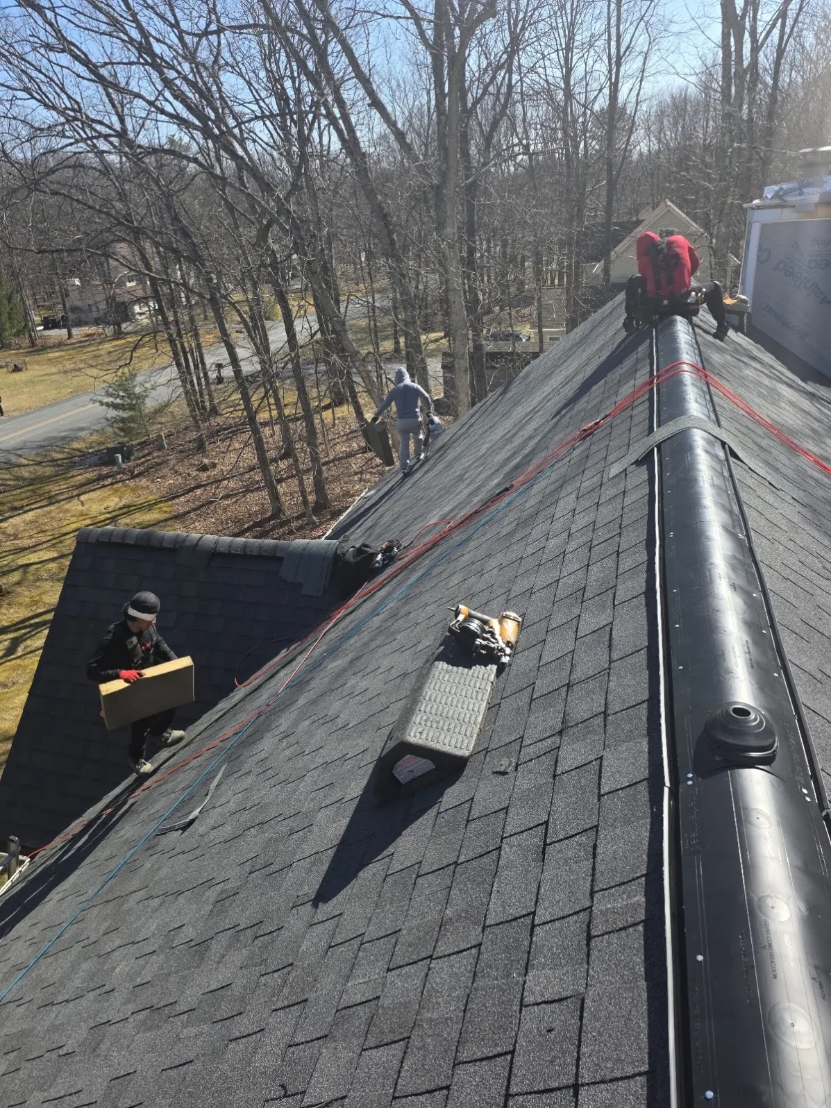 Three-person crew installing shingles and ridge vent on a Monroe County roof replacement