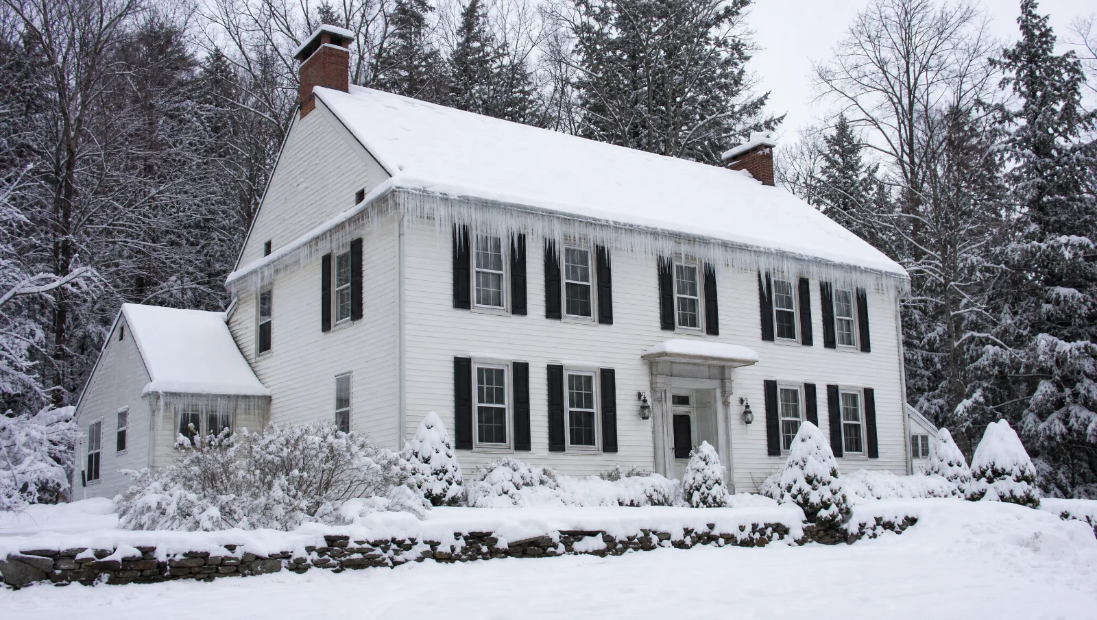 Snow-covered colonial house in the Poconos with a thick ridge of ice and long icicles along the gutters and eaves