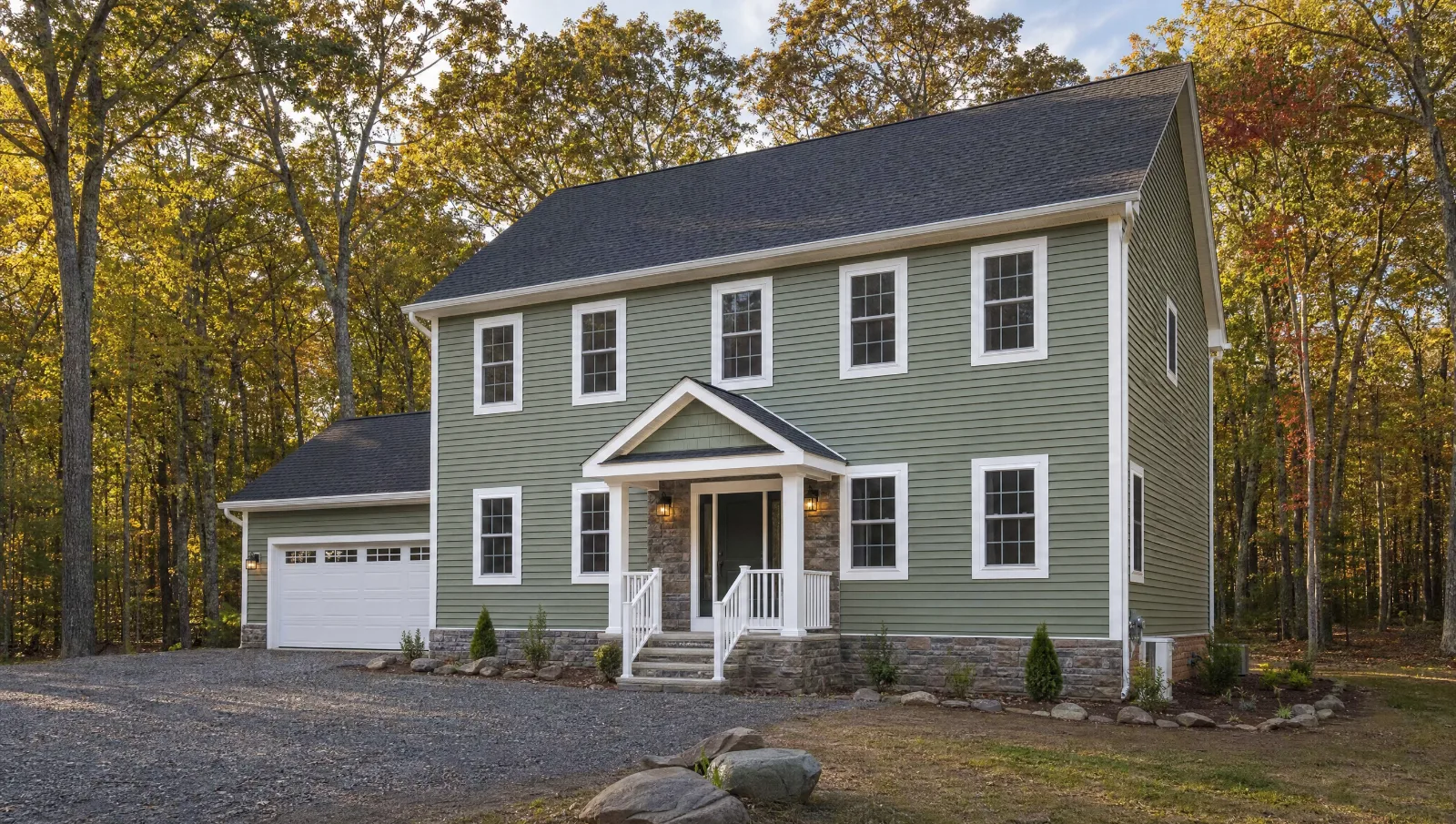 Two-story colonial in a wooded Poconos lot with sage green vinyl siding, white trim and a charcoal shingle roof